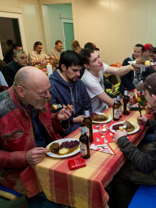 Eine Weihnachtsfeier für Wohnungslose in einer Obdachlosenunterkunft. Eine Frau reicht einen Teller mit Klößen, Fleisch und Rotkraut.