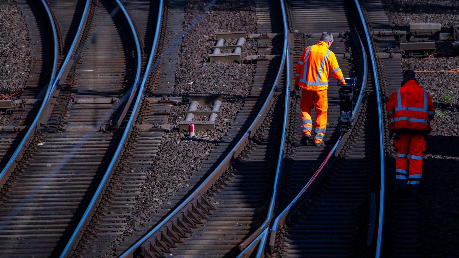 Bauarbeiter in orangefarbener Kleidung vermessen eine Schiene auf der Bahnstrecke Ludwigslust - Wismar. 