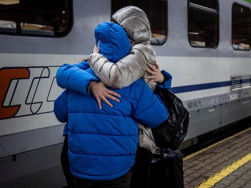 Drei Personen in Pufferjacken stehen vor eienm Zug und umarmen sich fest.