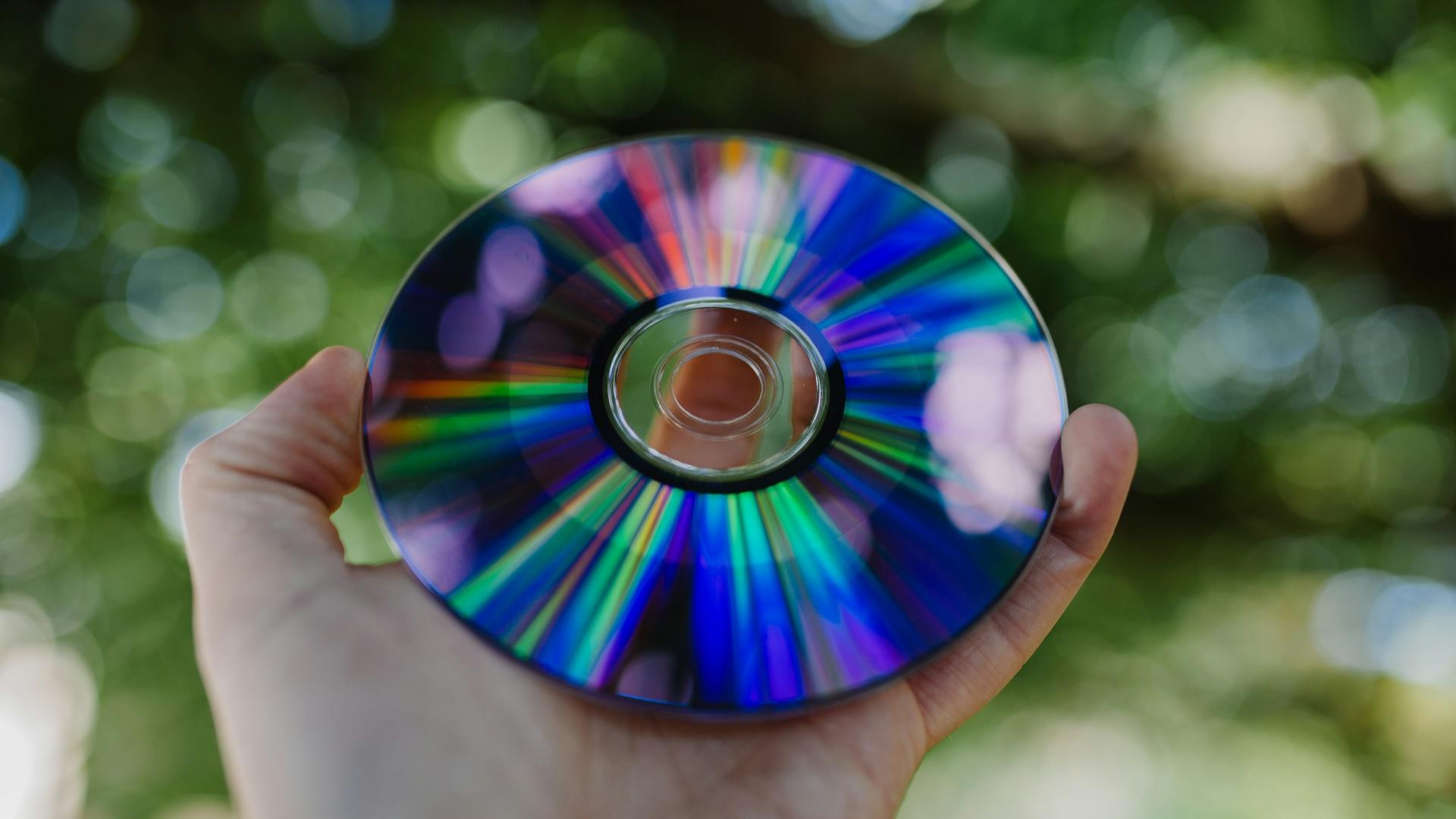 Ein Mann hält eine CD in der Hand, in der sich Regenbogenfarben zeigen. 