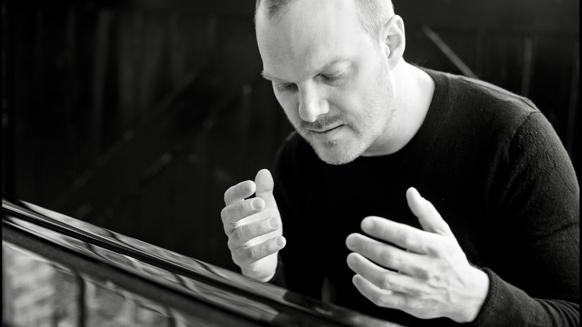 Der Pianist Lars Vogt sitzt am Flügel und hat beide Hände in einer Musikpause erhoben und genießt den Augenblick mit geschlossenen Augen.