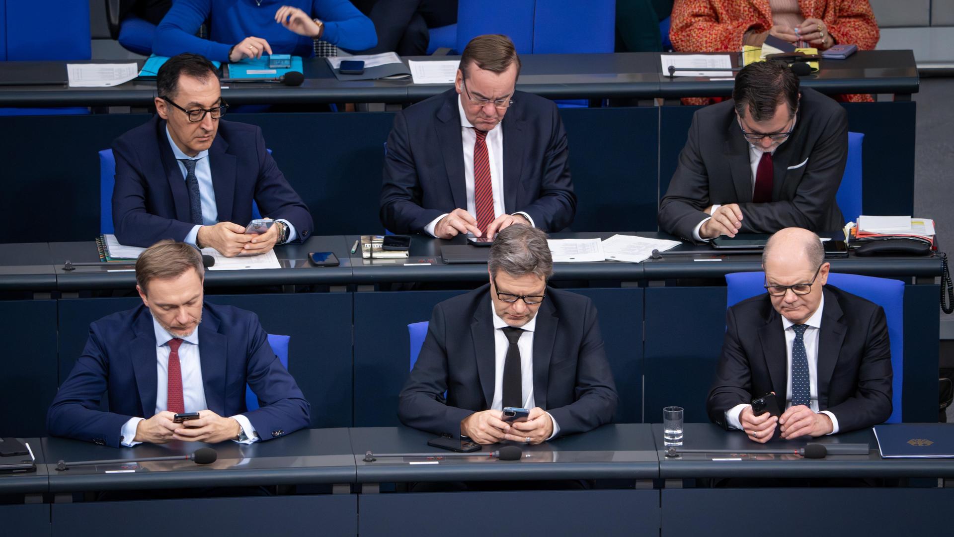 Mehrere Personen sitzen im Bundestag an langen Tischen und schauen in ihr Smartphone. 