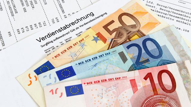 Gehaltszettel einer Person, darauf liegen Geldscheine (50-, 20- und 10-Euro-Schein)