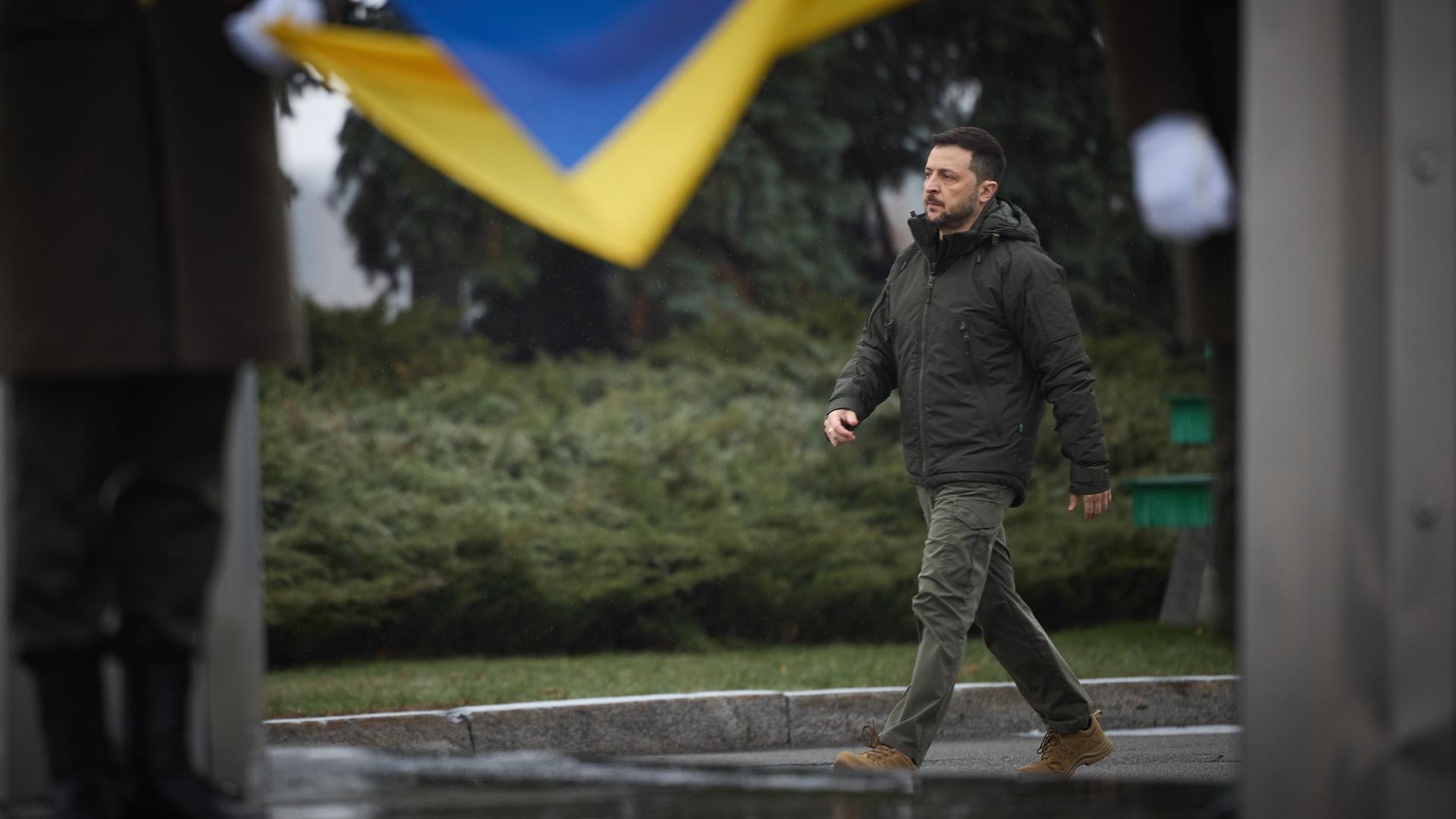 Der ukrainische Präsident Wolodymyr Selenskyj läuft am Tag der Streitkraefte der Ukraine am 06.12.2024 an einer Landes-Flagge vorbei.