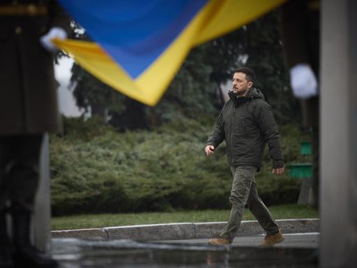 Der ukrainische Präsident Wolodymyr Selenskyj läuft am Tag der Streitkraefte der Ukraine am 06.12.2024 an einer Landes-Flagge vorbei.