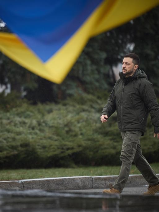 Der ukrainische Präsident Wolodymyr Selenskyj läuft am Tag der Streitkraefte der Ukraine am 06.12.2024 an einer Landes-Flagge vorbei.