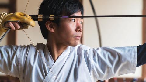 Porträt eines jungen japanischen Mannes, der konzentriert seinen Bogen aufspannt.