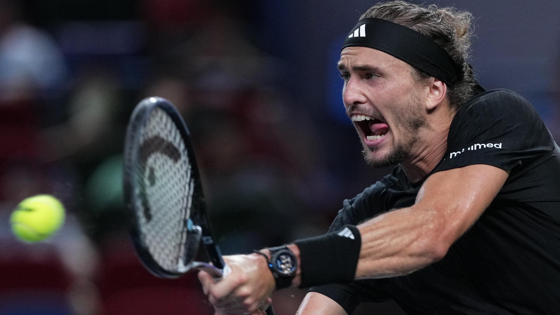 Alexander Zverev beim Tennis-Turnier in Shanghai; er trägt ein schwarzes T-Shirt sowie ein Stirnband und Schweißbänder und schlägt mit beiden Händen einen Ball.