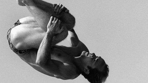 Schwarzweißfoto von Jan Hempel beim Turmspringen. Seine Körperhaltung mit angezogenen Gliedmaßen erinnert an die Embryonalstellung.
