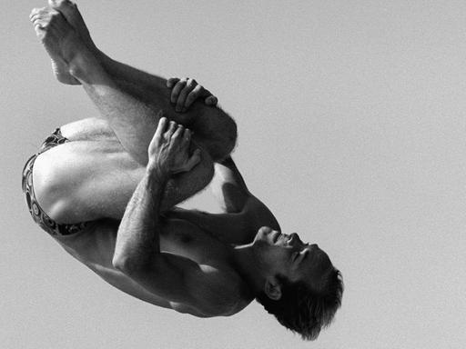 Schwarzweißfoto von Jan Hempel beim Turmspringen. Seine Körperhaltung mit angezogenen Gliedmaßen erinnert an die Embryonalstellung.