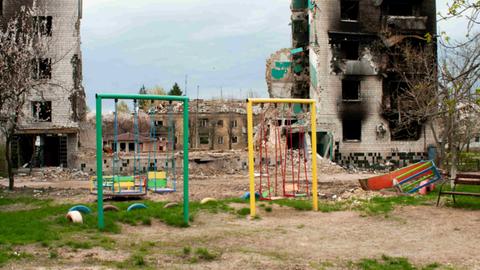 Ein bunter Spielplatz vor ausgebrannten Häuserruinen in der Ukraine Ein bunter Spielplatz vor ausgebrannten Häuserruinen in der Ukraine