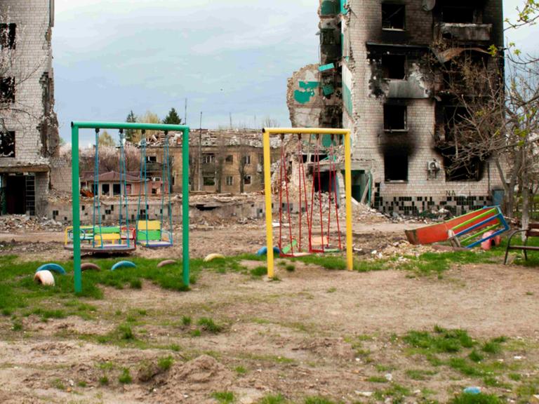 Ein bunter Spielplatz vor ausgebrannten Häuserruinen in der Ukraine Ein bunter Spielplatz vor ausgebrannten Häuserruinen in der Ukraine