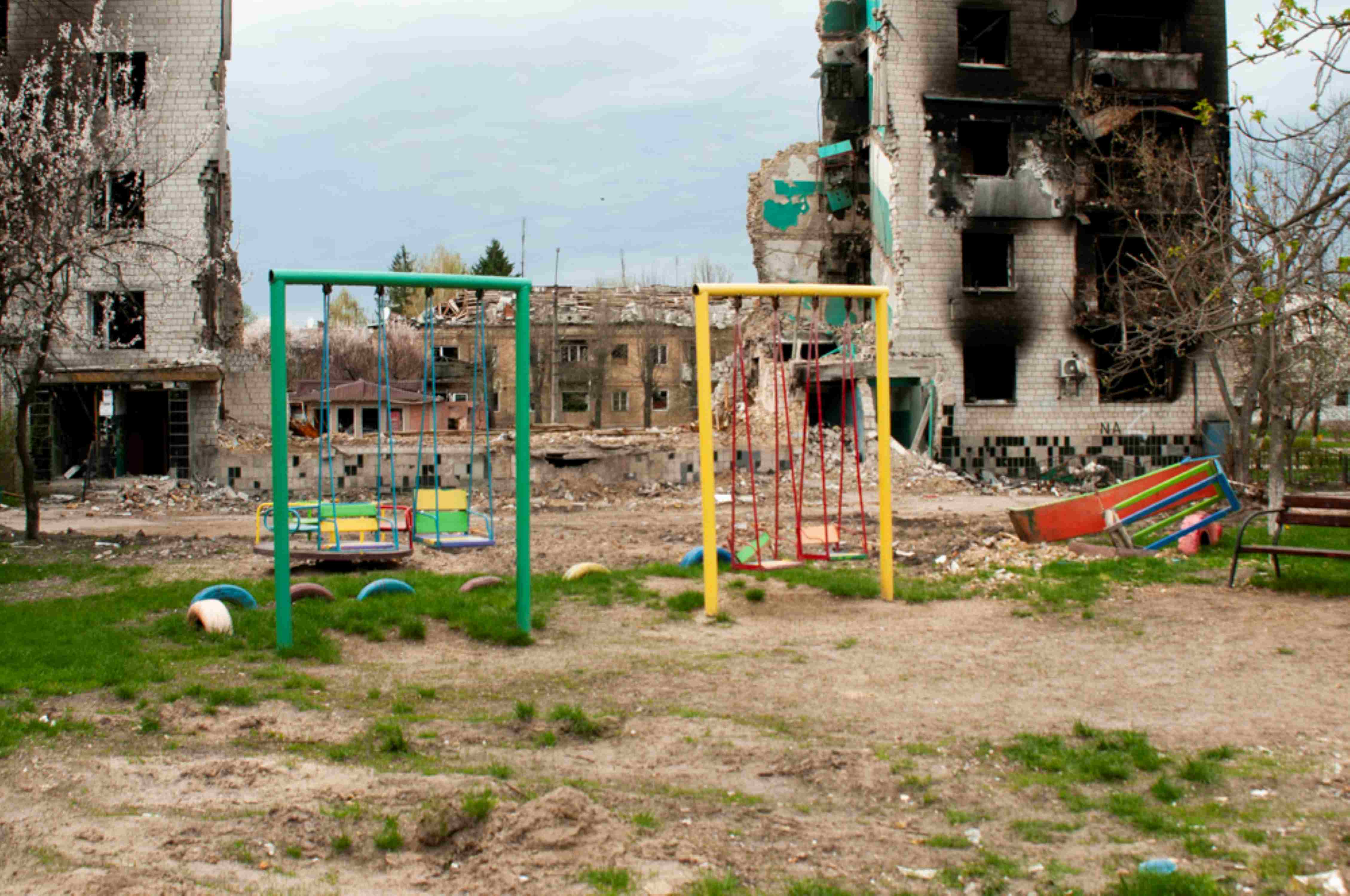 Ein bunter Spielplatz vor ausgebrannten Häuserruinen in der Ukraine