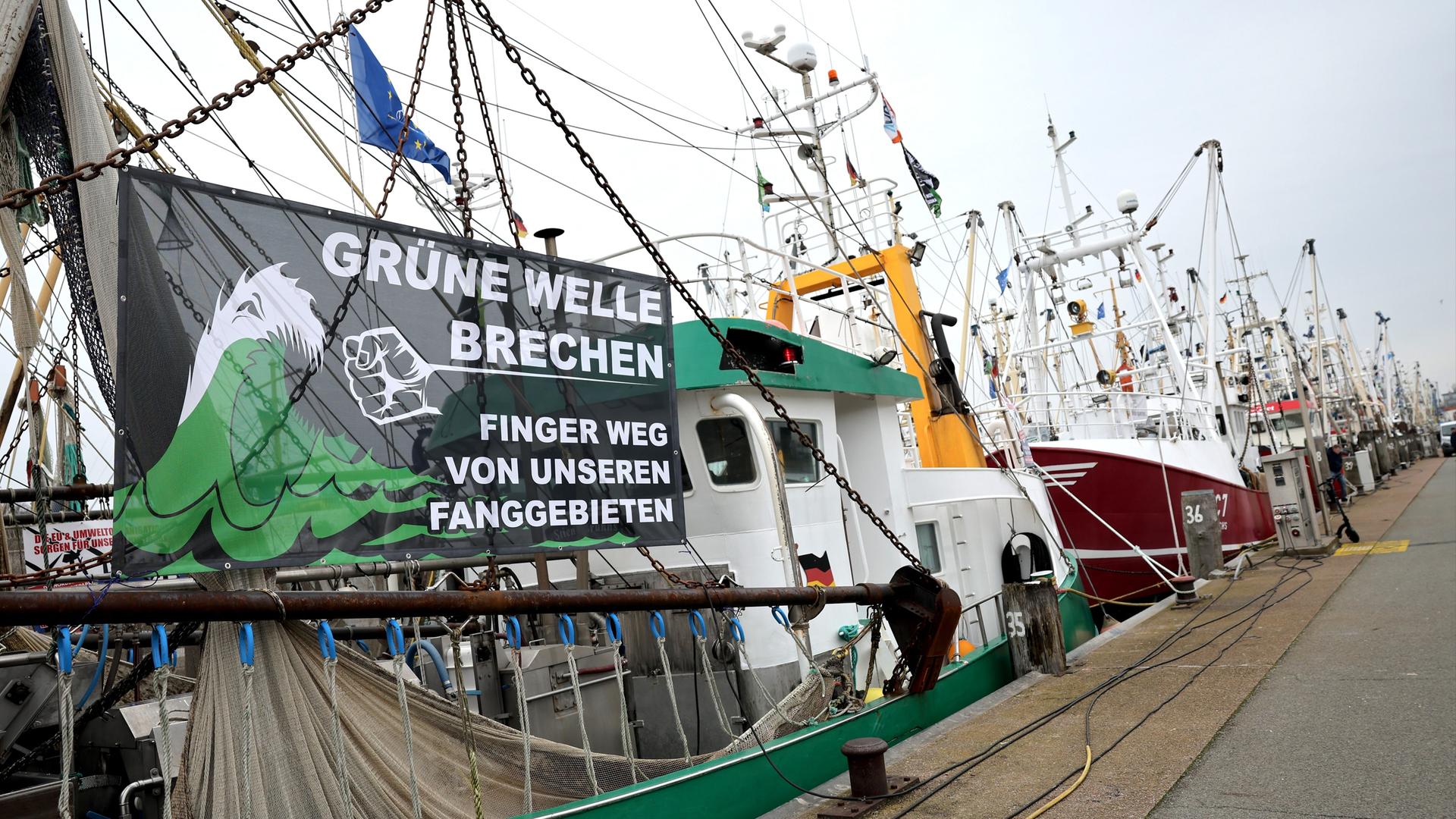 Ein Protestbanner mit dem Text "Grüne Welle brechen - Finger weg von unseren Fanggründen" ist an einem Kutter im Hafen von Büsum zu sehen.