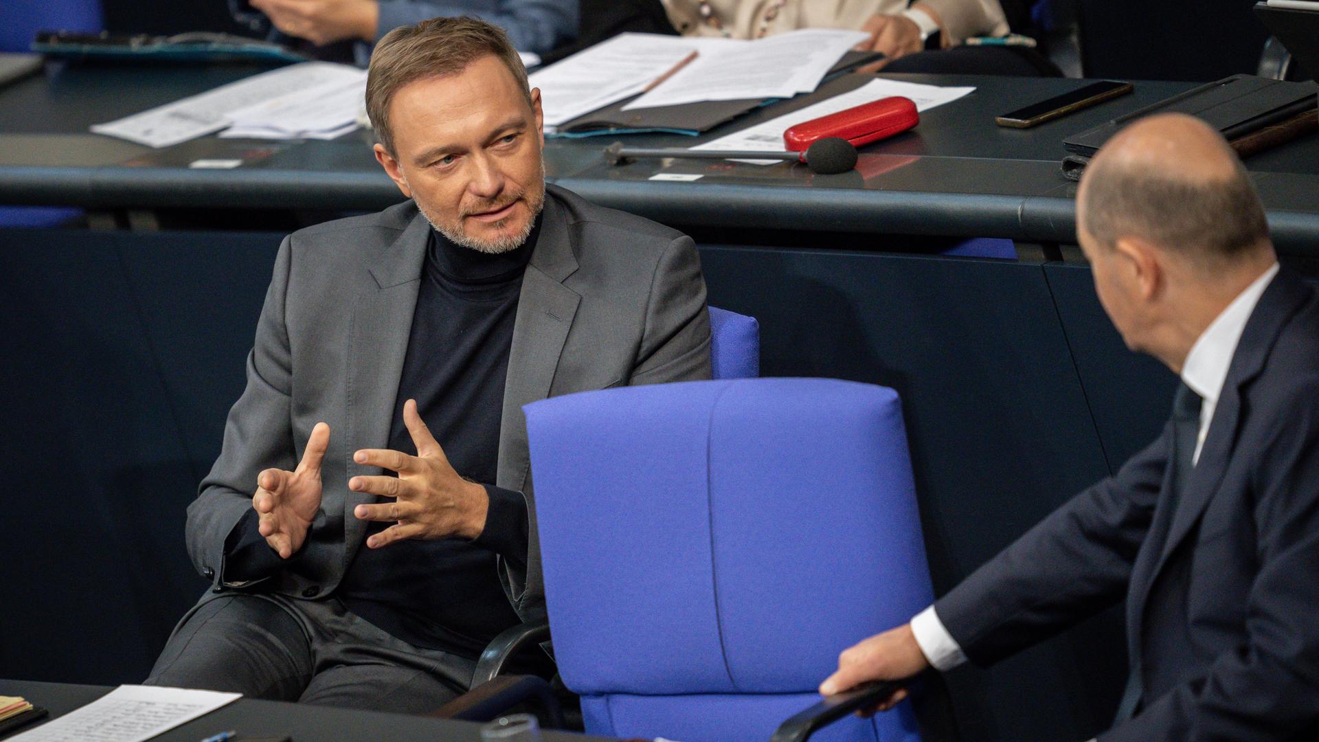 Das Foto zeigt Bundesfinanzminister Lindner neben Bundeskanzler Scholz auf der Regierungsbank im Bundestag. Lindner spricht mit Scholz und gestikuliert dabei mit seinen Händen.
