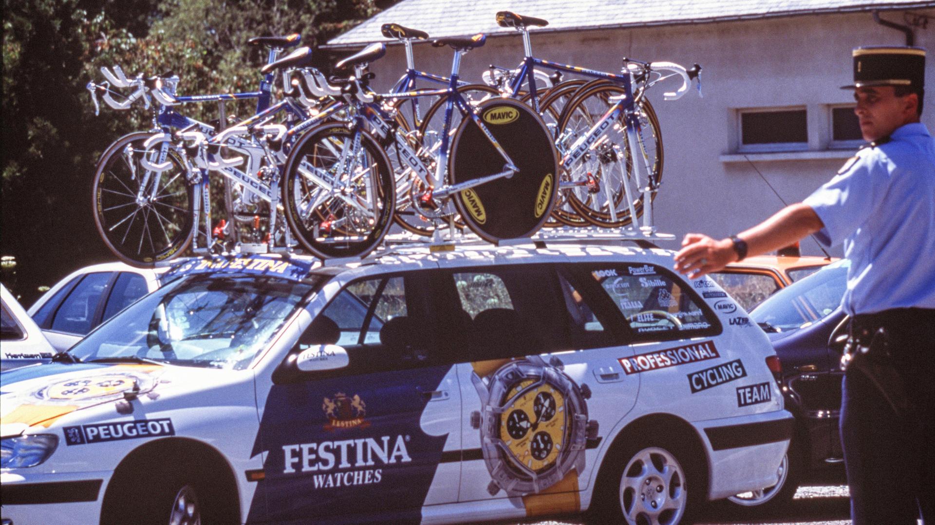 Tour de France 1998: Ein Fahrzeug des Teams Festina mit Rädern auf dem Dach wird von einem Polizisten eingewiesen. 