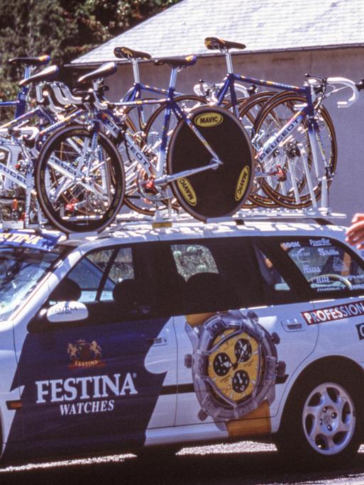 Tour de France 1998: Ein Fahrzeug des Teams Festina mit Rädern auf dem Dach wird von einem Polizisten eingewiesen. 