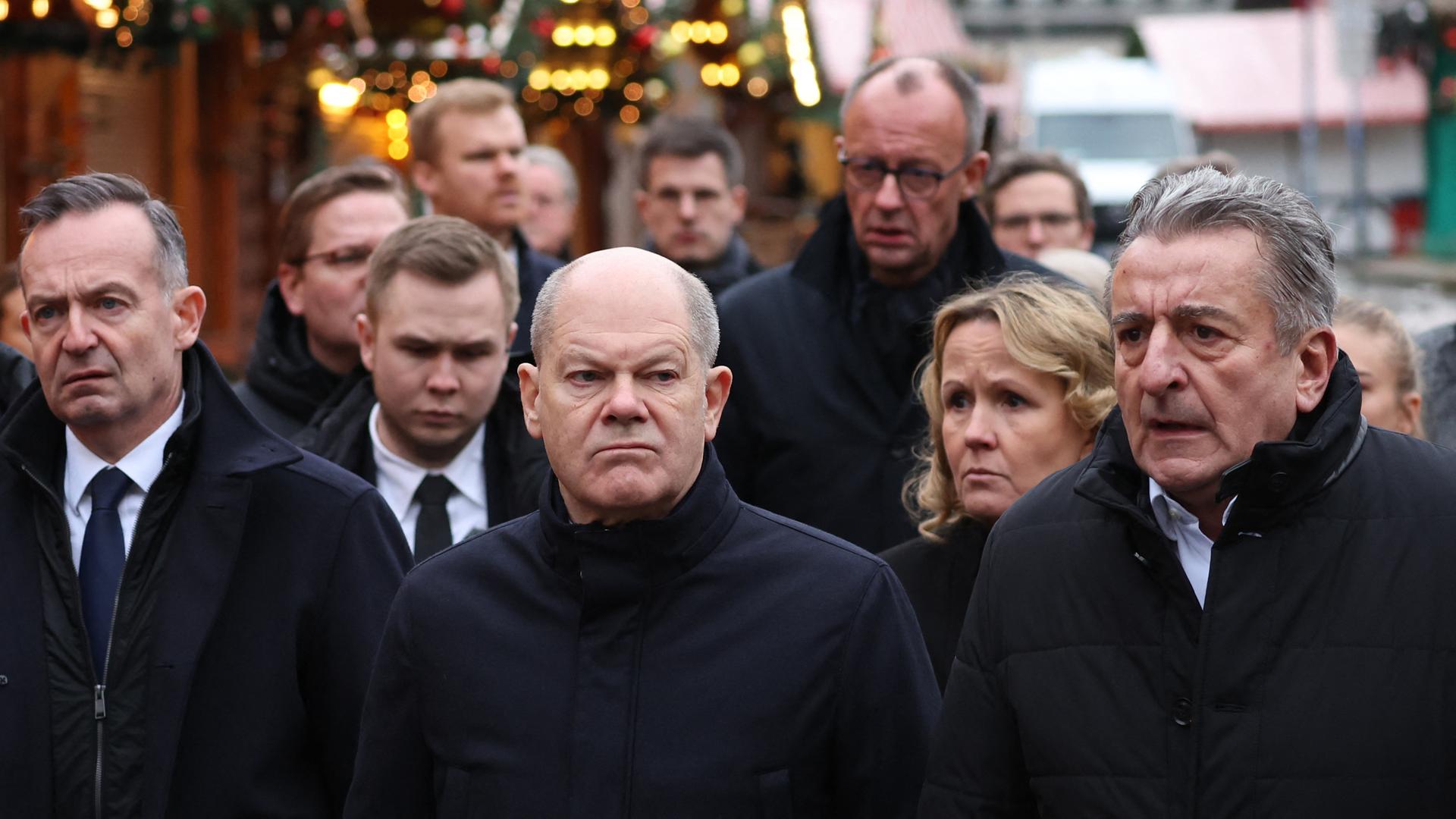 Scholz und andere Politiker zeigen sich mit ernsten Gesichtsausdrücken auf dem Weihnachtsmarkt.