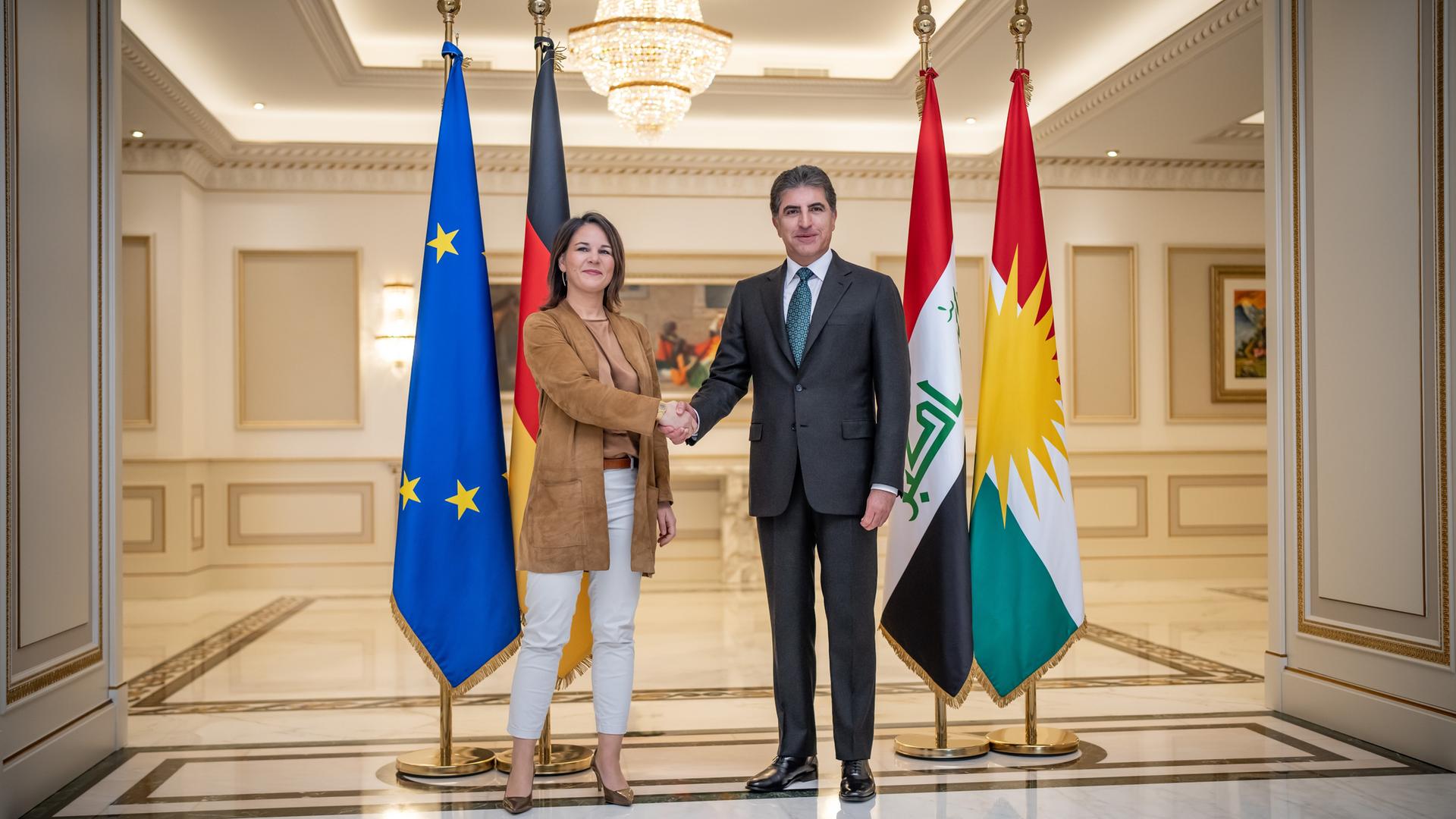 Annalena Baerbock (Bündnis90/Die Grünen), Bundesaußenministerin, steht neben Nechirvan Barsani, Präsident der Region Kurdistan-Irak, der kurdischen Autonomiegebiete im Nordirak. Sie schütteln sich die Hände. Sie stehen in einem hell erleuchteten Saal. Hinter Baerbock sieht man die Flagge von Deutschland und der Europäischen Union. Hinter Barsani stehen die Flaggen vom Irak und Kurdistan.