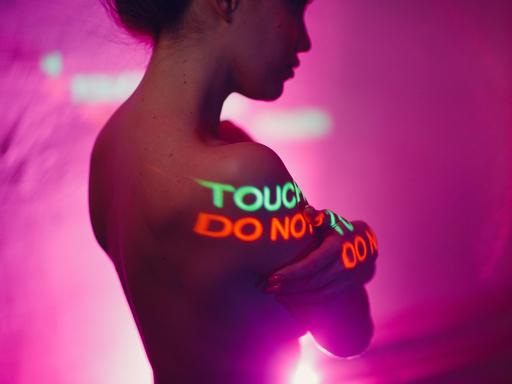 Eine Frau steht oberkörperfrei, während auf ihren Körper "Do not touch" (dt. "Nicht anfassen") projeziert wird.