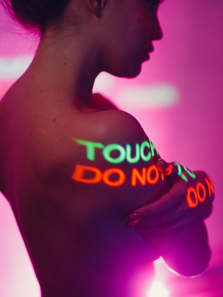Eine Frau steht oberkörperfrei, während auf ihren Körper "Do not touch" (dt. "Nicht anfassen") projeziert wird.