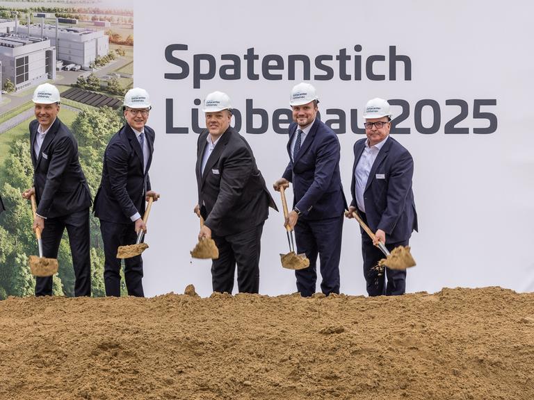 Spatenstich für das Rechenzentrum in Lübbenau. Männer im dunklen Anzug mit Helm auf dem Kopf und Schaufel in der Hand vor einem Schild "Spatenstich Lübbenau"  