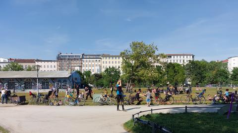 Der Görlitzer Park in Berlin-Kreuzberg bei sommerlichen Temperaturen. Im Vordergrund Besucherinnen und Besucher des Parks, im Hintergrund eine Häuserfront.