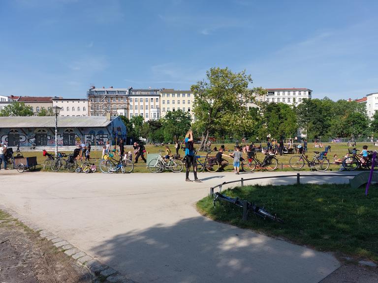 Der Görlitzer Park in Berlin-Kreuzberg bei sommerlichen Temperaturen. Im Vordergrund Besucherinnen und Besucher des Parks, im Hintergrund eine Häuserfront.