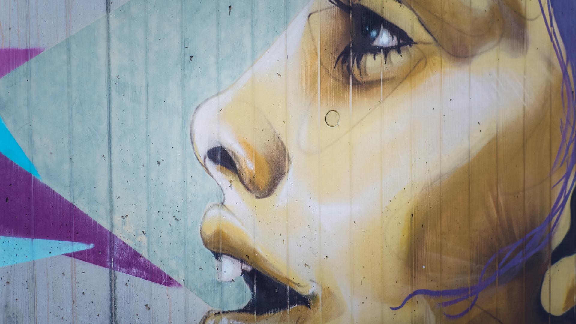 Graffiti auf einer Mauer, das eine junge Frau mit geöffnetem Mund zeigt, als ob sie singen würde.