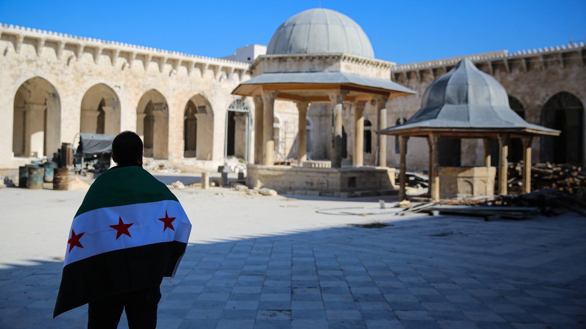 Eine Person steht mit der neuen syrischen Flagge auf dem Innenhof der beschädigten Umayyaden-Moschee in Aleppo.