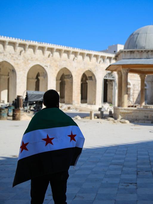 Eine Person steht mit der neuen syrischen Flagge auf dem Innenhof der beschädigten Umayyaden-Moschee in Aleppo.