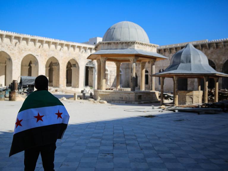 Eine Person steht mit der neuen syrischen Flagge auf dem Innenhof der beschädigten Umayyaden-Moschee in Aleppo.