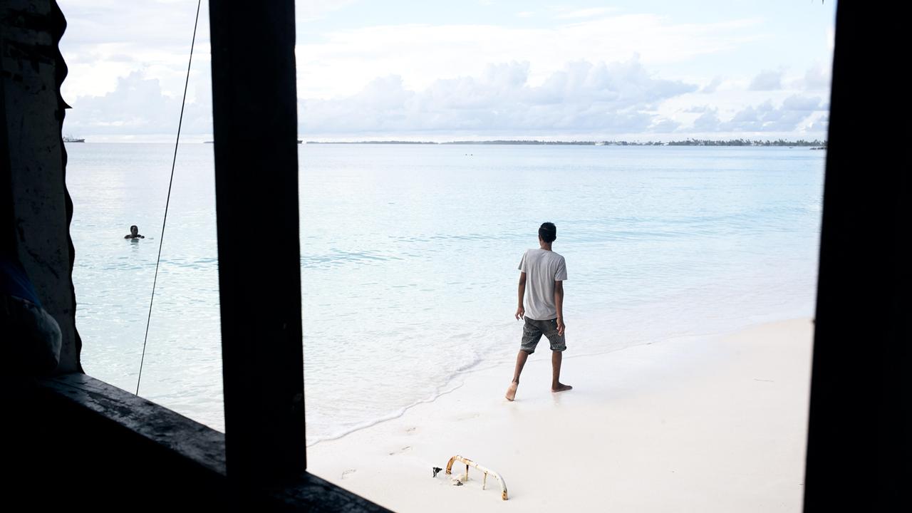 Durch das Fenster eines direkt am Strand stehenden Hauses ist ein Mann zu sehen, der den Strand entlang läuft.