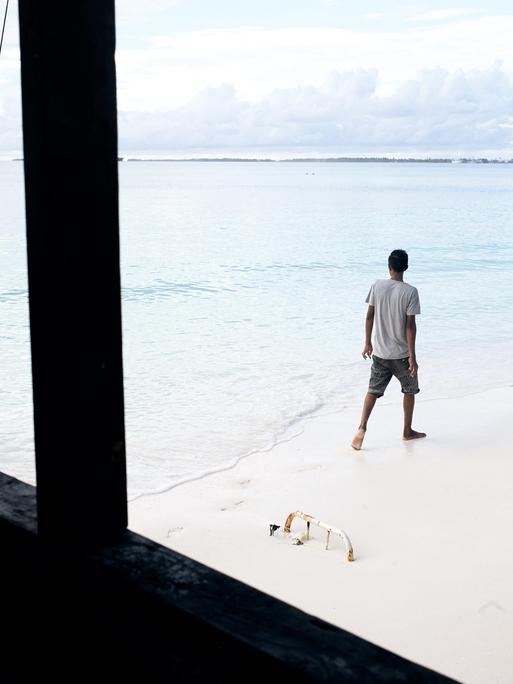 Durch das Fenster eines direkt am Strand stehenden Hauses ist ein Mann zu sehen, der den Strand entlang läuft.