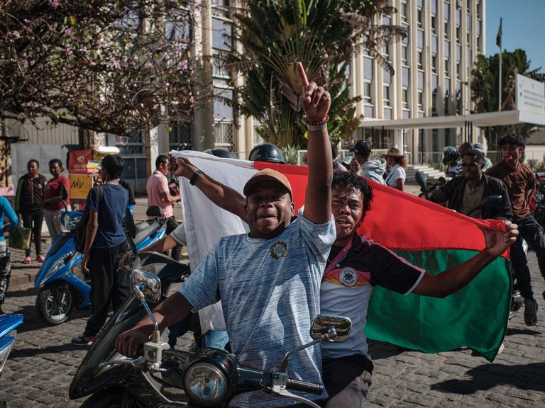Junge Menschen auf kleinen Motorrädern und Motorrollern in Madagaskar. Sie schwenken Flaggen und protestieren gegen die Regierung.
