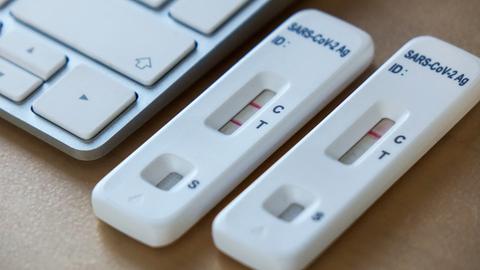Positiver und negativer Coronatest neben einer Tastatur am Arbeitsplatz.
