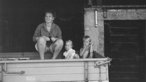 Gabriele sitzt mit zwei Kindern auf einem Hänger, der in einer Scheune steht