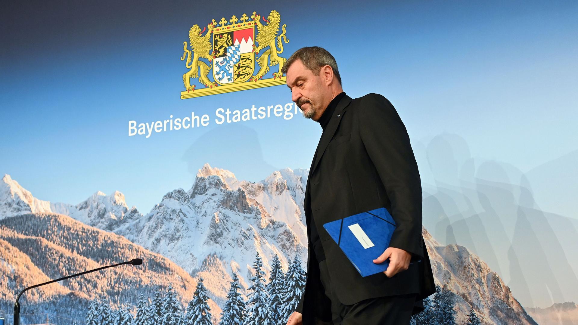 Bayerns Ministerpräsident Markus Söder (CSU) geht an einen Tisch während einer Presskonferenz. Im Hintergrund ist eine winterliche Alpenkulisse zu sehen. Bayerns Ministerpräsident Markus Söder (CSU) geht an einen Tisch während einer Presskonferenz. Im Hintergrund ist eine winterliche Alpenkulisse zu sehen.