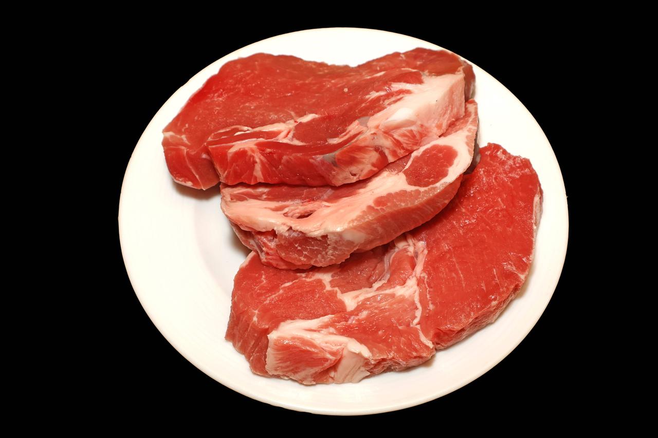 Auf einem weißen flachen Teller liegen zwei rohe Schweine-Nackensteaks. Auf einem weißen flachen Teller liegen zwei rohe Schweine-Nackensteaks.