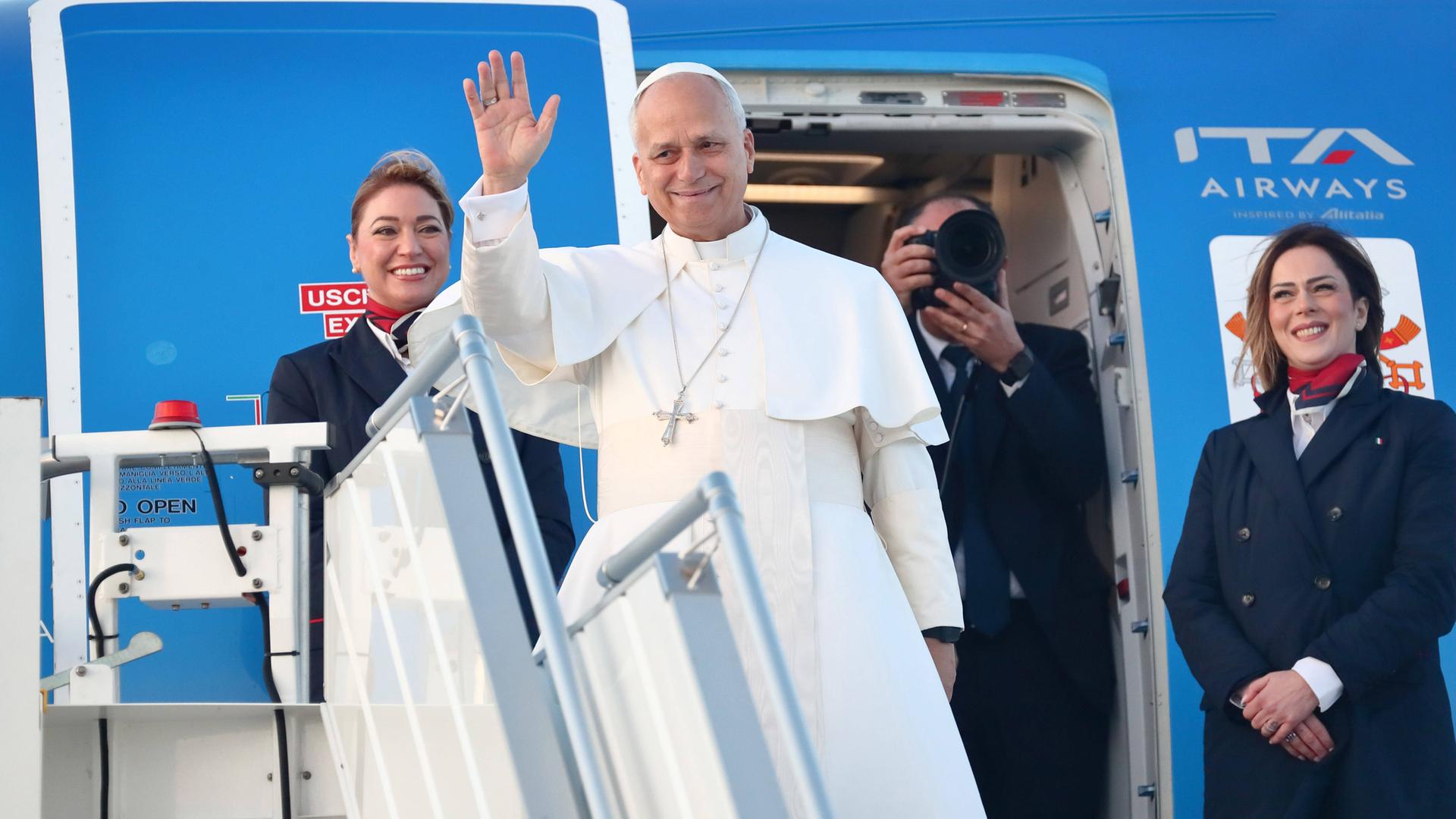 Papst Leo XIV. geht an Bord eines Flugzeugs und winkt, neben ihm stehen zwei Flugbegleiterinnen