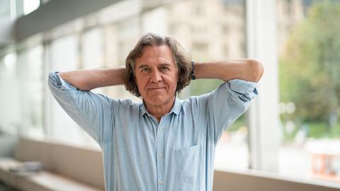 De Krimiautor Norbert Scheuer steht am 29.9.2019 anlässlich der Verleihung des Deutschen Buchpreises im Foyer eines Theaters in Frankfurt. Er trägt ein helles Hemd und hat die Arme hinter dem Kopf verschränkt.