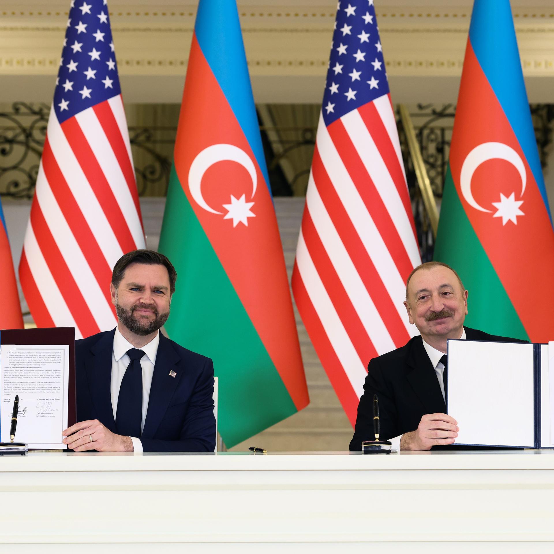 US-Vizepräsident JD Vance (l) und der aserbaidschanische Präsidenten Ilham Alijew sitzen vor aserbaidschanischen und US-amerikanischen Flaggen. Sie halten unterzeichnete Verträge in ihren Händen.