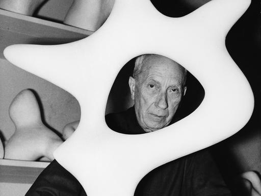 Der Maler, Bildhauer und Lyriker Hans Arp (1886-1966) schaut in seinem Atelier durch eine seiner Plastiken. 