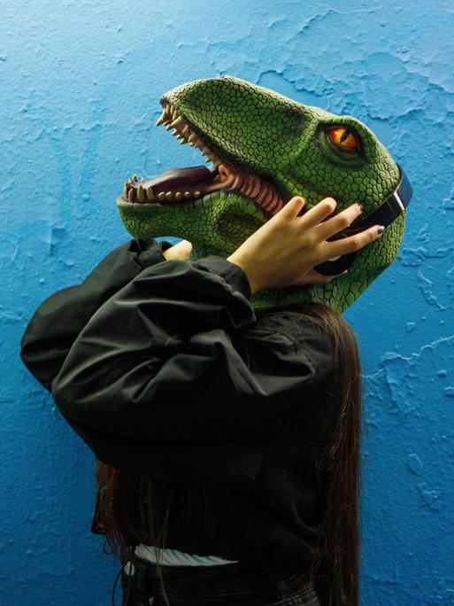 Zwei Menschen mit Dinosauriermaske tragen Kopfhörer und hören Podcasts.