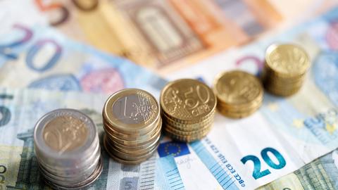 Münzen und Euro-Banknoten liegen auf einem Tisch.
