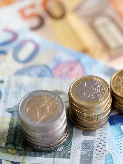 Münzen und Euro-Banknoten liegen auf einem Tisch.