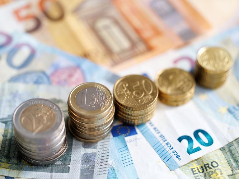 Münzen und Euro-Banknoten liegen auf einem Tisch.