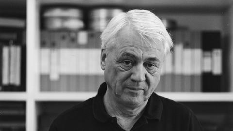 Schwarzweiße Porträtaufnahme zeigt Alexander Kluge vor einem Bücherregal mit Filmrollen im Jahr 1997