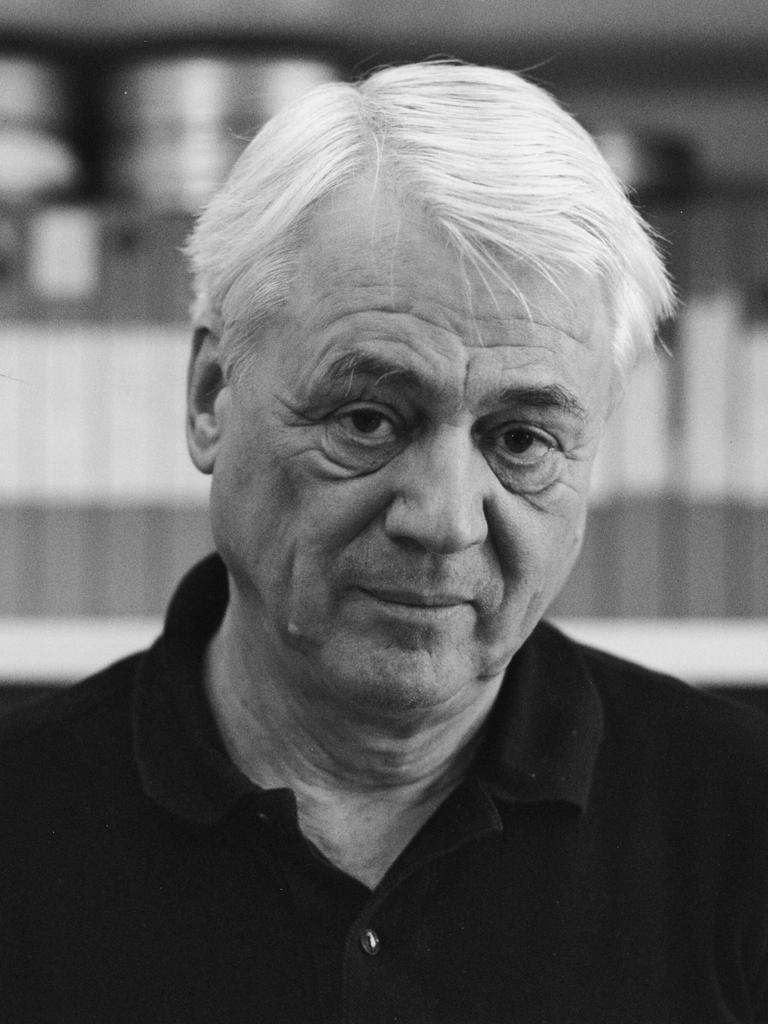 Schwarzweiße Porträtaufnahme zeigt Alexander Kluge vor einem Bücherregal mit Filmrollen im Jahr 1997