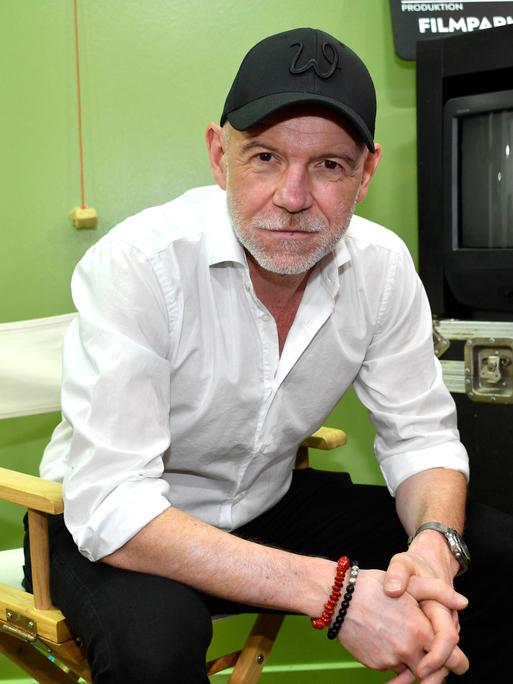 Dietmar Wunder sitzt in einem Studio im Filmpark Babelsberg auf einem Regiestuhl und schaut freundlich in die Kamera